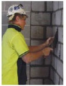 A Bricklayer removing excess mortar using a hand trowel