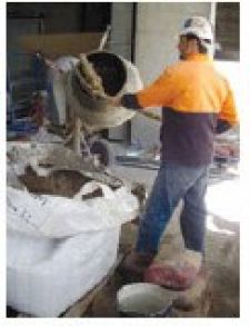 A Bricklayer shovelling sand and ingredients into mixer